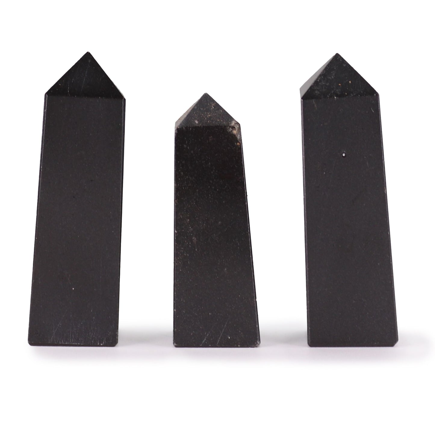 Hand-carved and polished black tourmaline gemstone obelisk point standing on a plain surface.