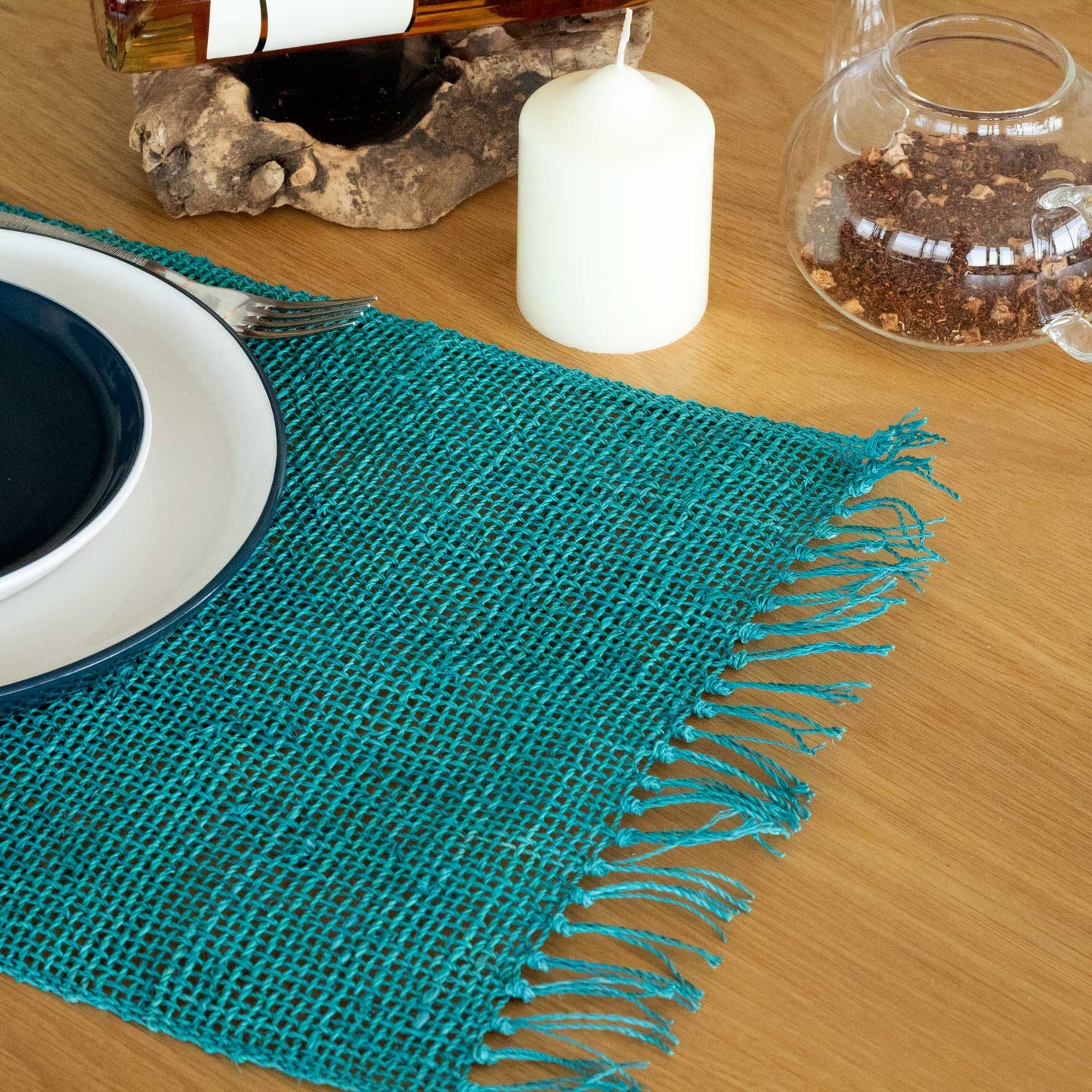 Handcrafted round natural seagrass placemat with a vibrant turquoise centre and decorative fringe edging.