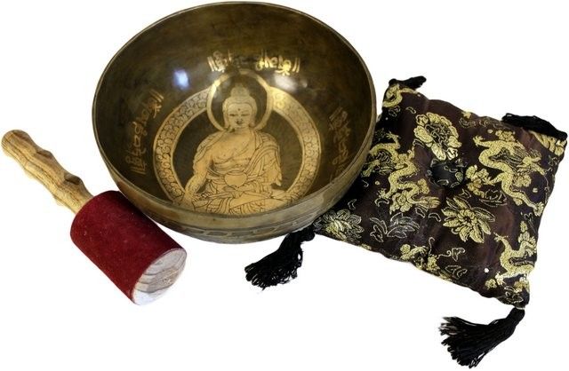 Golden brass singing bowl with Buddha engraving, resting on a decorative cushion next to a suede-coated wooden striker.