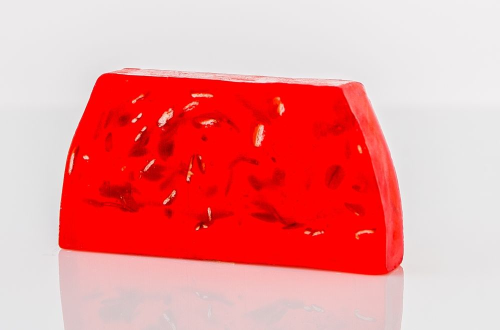 A thick slice of handmade pomegranate soap showing a rich red colour and textured surface.