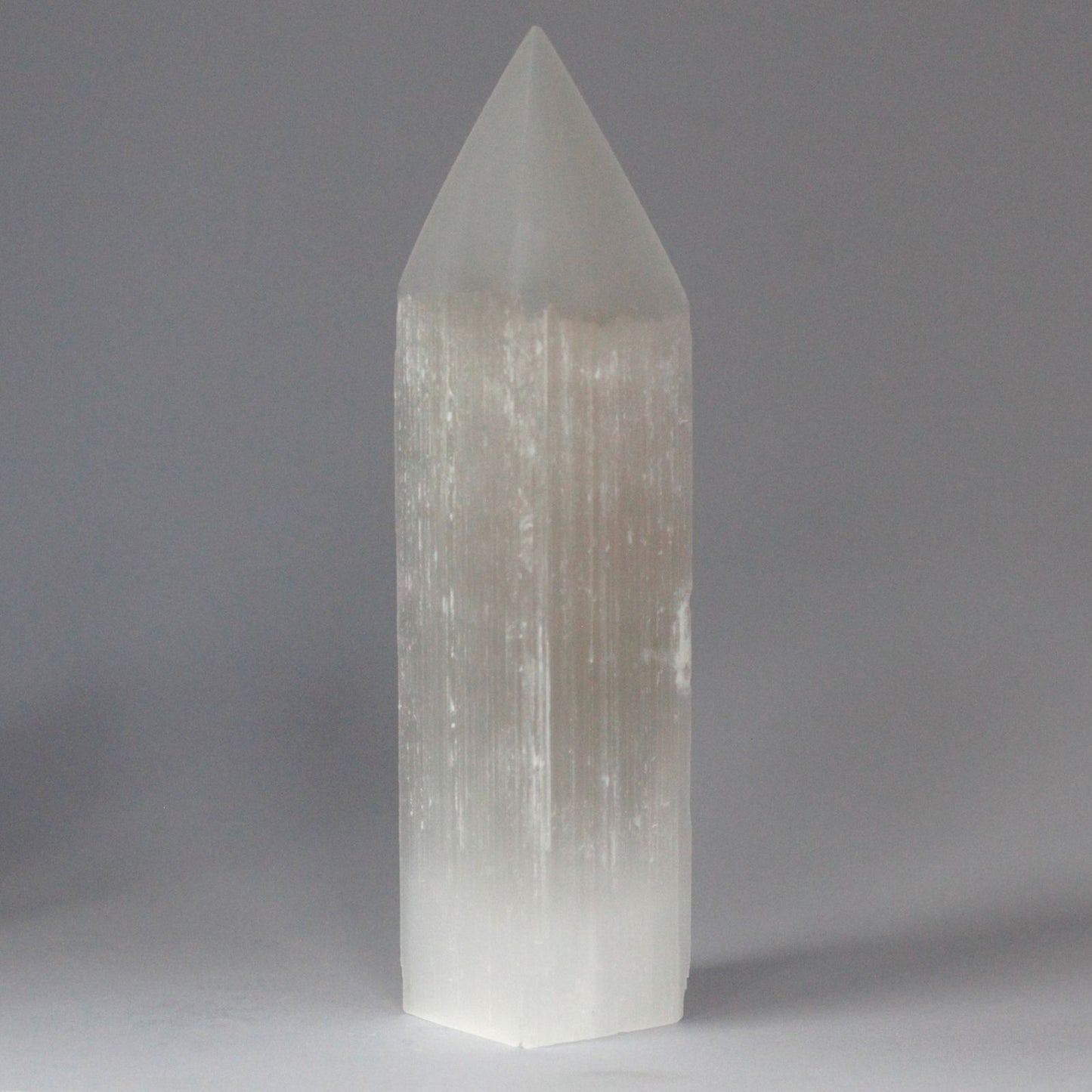 Tall translucent white Selenite crystal tower with a pointed pencil tip and natural milky texture reflecting light.