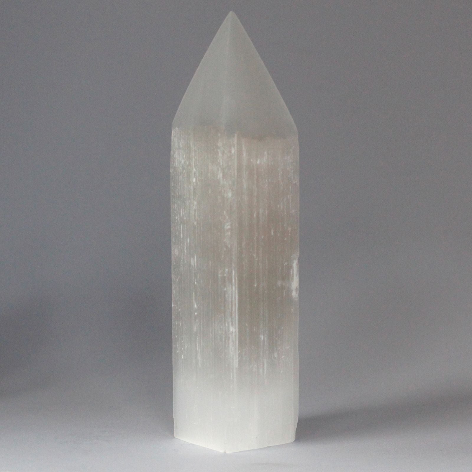 Tall translucent white Selenite crystal tower with a pointed pencil tip and natural milky texture reflecting light.