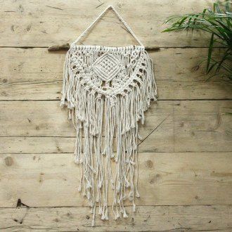 Handcrafted cream macrame wall hanging with intricate heart-shaped knotting on a natural wooden branch.
