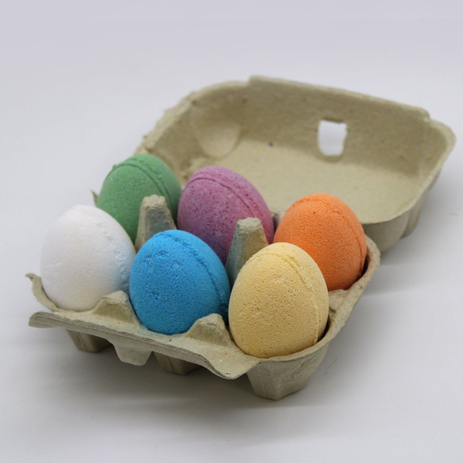 A tray of six colourful, egg-shaped bath bombs with various scents and speckled textures.