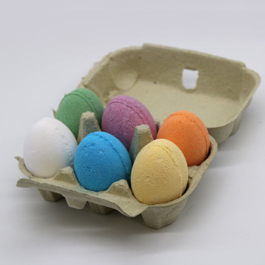A tray of six colourful, egg-shaped bath bombs with various scents and speckled textures.