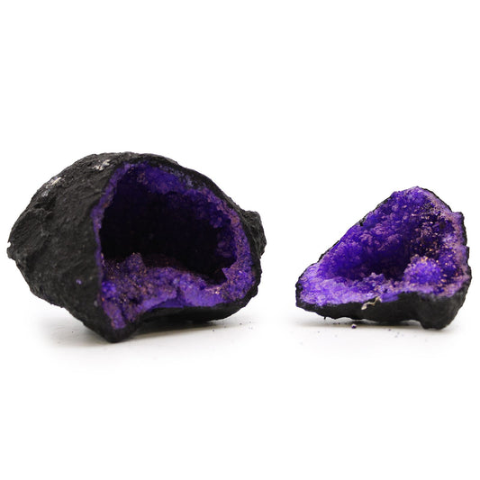 A split black rock geode revealing vibrant artificially coloured purple calcite crystals inside.