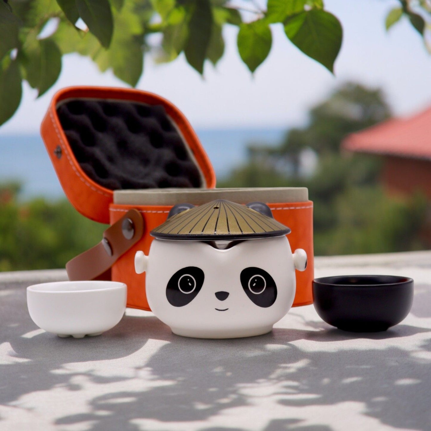 Whimsical ceramic teapot featuring a panda face with two matching cups in a compact black travel carrying case.