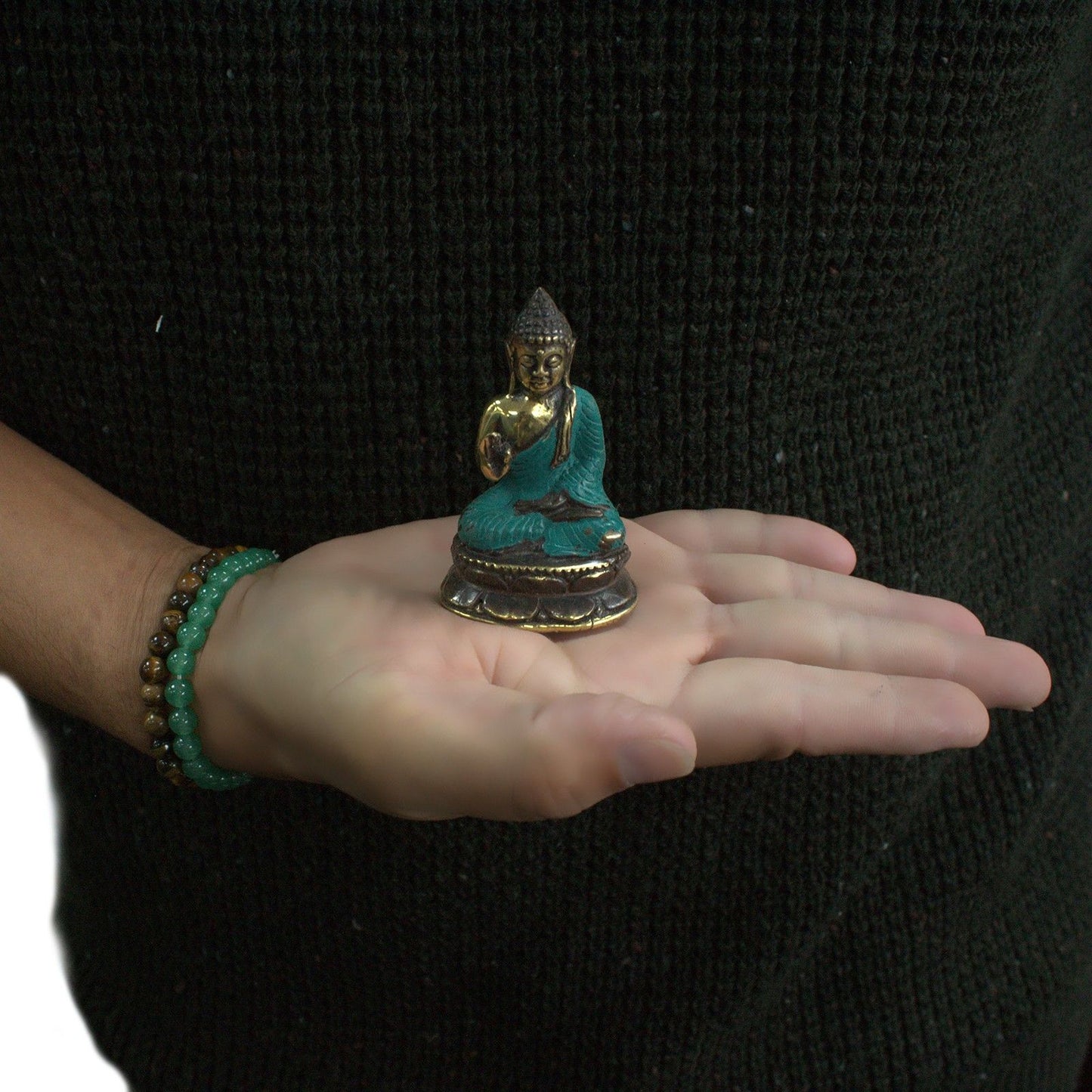 Small brass statue of a sitting Buddha with one hand raised in a traditional Eastern inspired design.