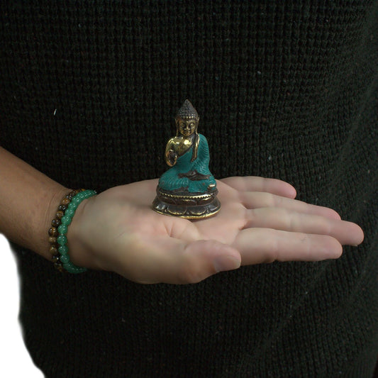 Small brass statue of a sitting Buddha with one hand raised in a traditional Eastern inspired design.