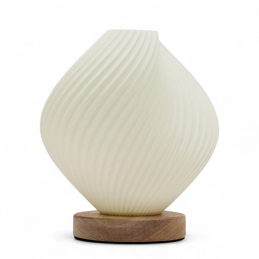 Graceful white spiral lamp with a shell-inspired twisted design emitting a soft warm glow in a modern interior setting.