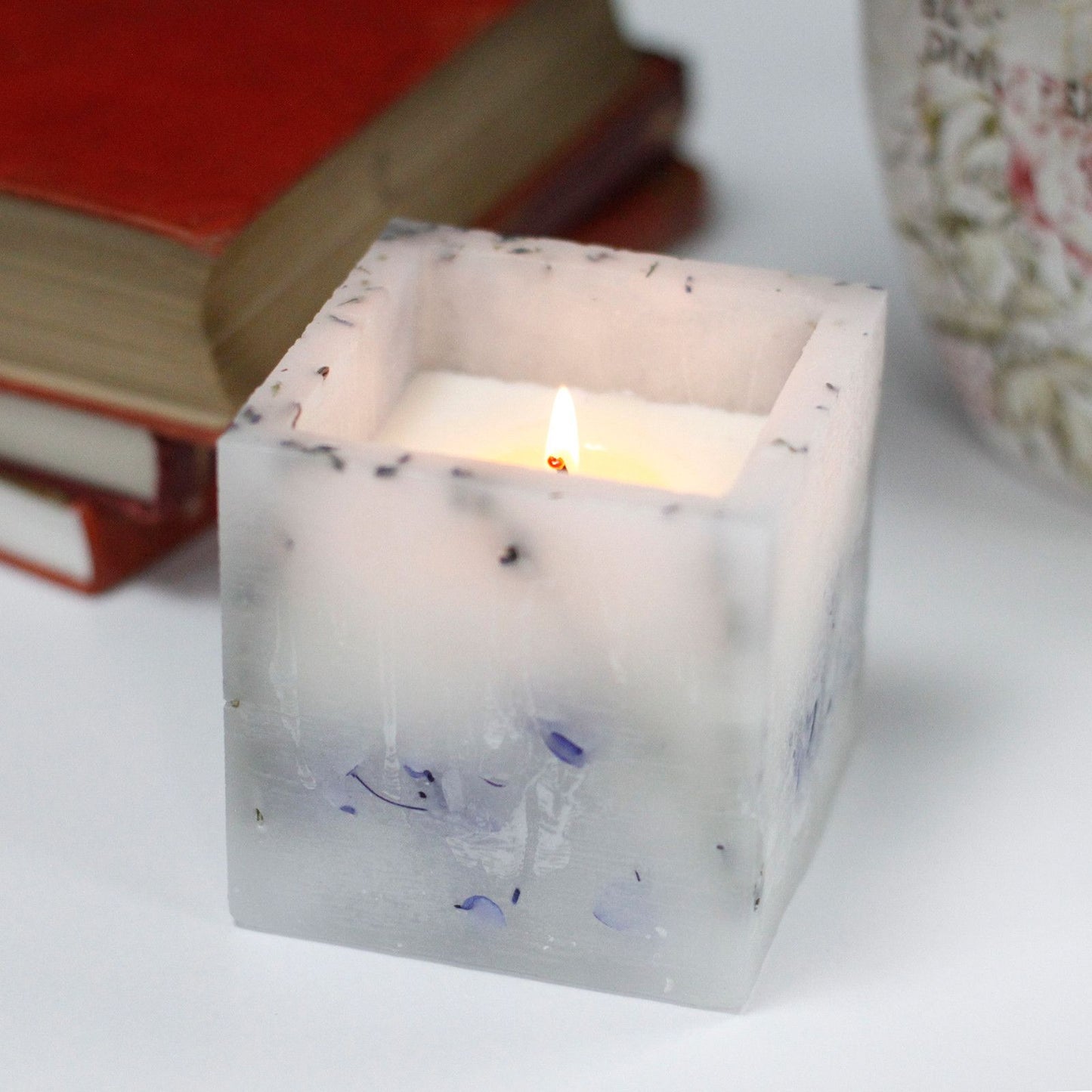 Large square purple candle with an enchanted glowing effect and dried lavender botanical inclusions.