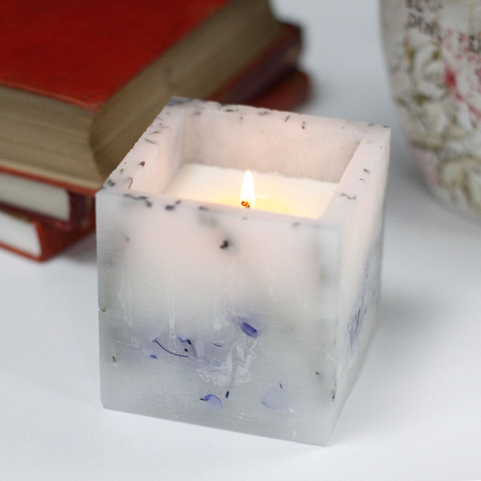 Large square purple candle with an enchanted glowing effect and dried lavender botanical inclusions.
