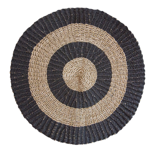 A round 1 metre seagrass rug featuring a natural tan base with a decorative black circular pattern.