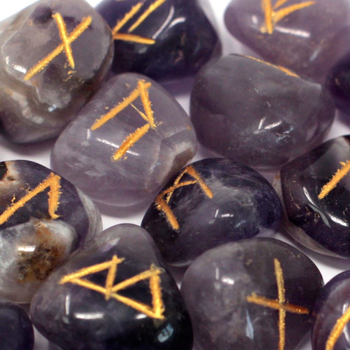 Tumbled amethyst stones engraved with traditional rune symbols laid out next to a small black drawstring pouch.