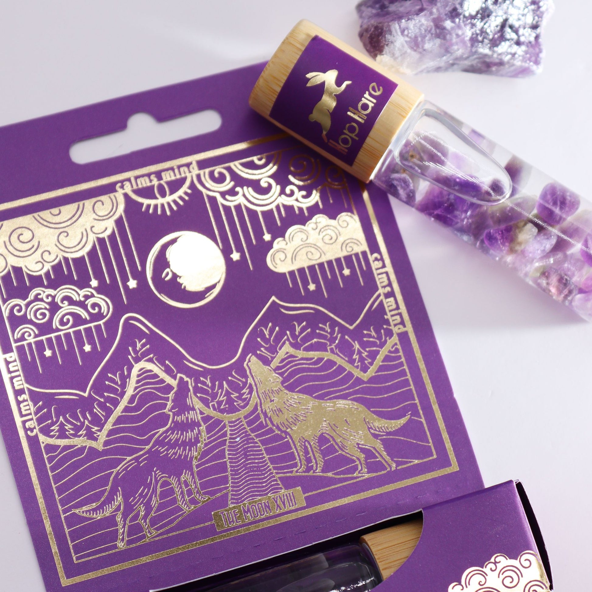 Cylindrical glass roll-on bottle with a tarot-inspired label featuring a moon design and purple amethyst gemstones inside.