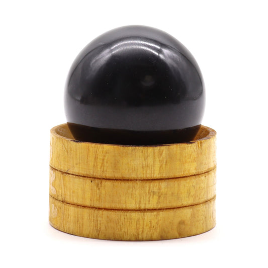 A polished dark tourmaline gemstone sphere resting on a small wooden stand, showing natural crystal textures.