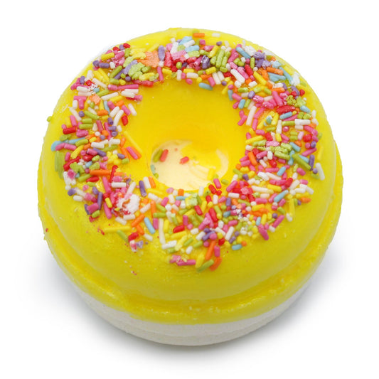 Two colourful bath fizzers shaped like donuts with yellow icing and white drizzle on a plain background.