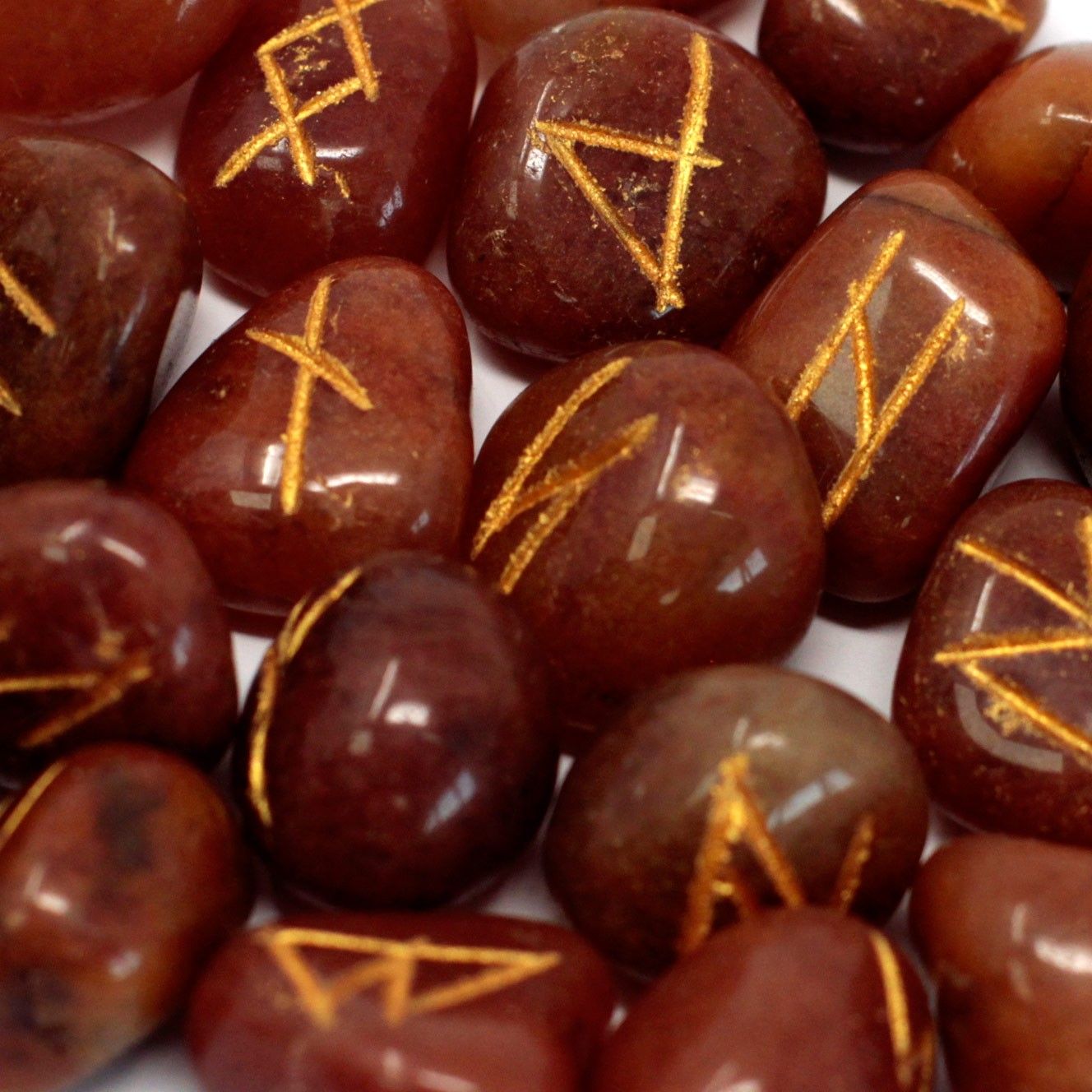 Red aventurine rune stones with gold-engraved symbols spread out next to a small black drawstring pouch.