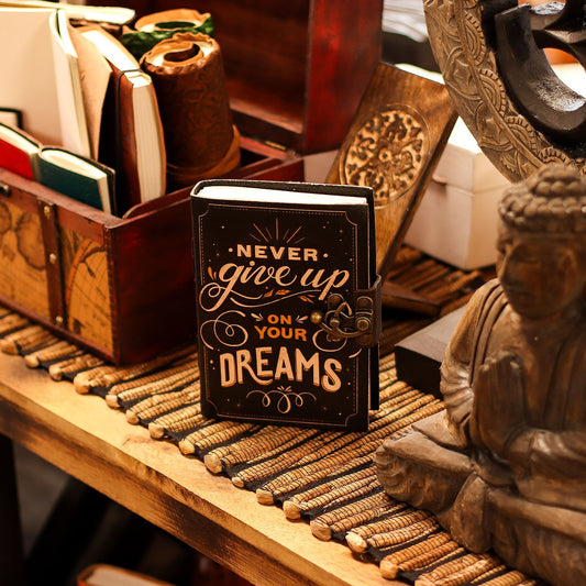 Vintage style brown leather notebook embossed with Never Give Up On Your Dreams quote and a traditional metal clasp closure.