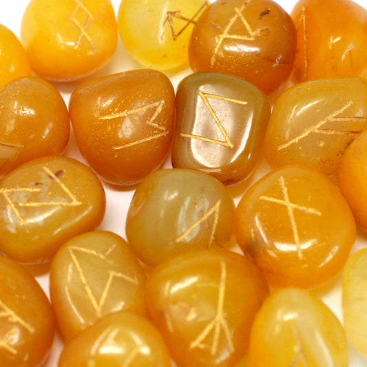 Set of polished yellow onyx rune stones engraved with black symbols, resting on a small velvet drawstring pouch.