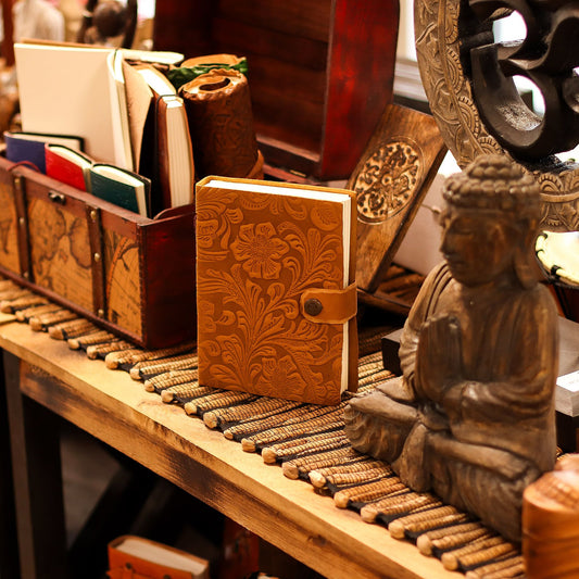 Handcrafted tan leather notebook with detailed floral embossing and rustic stitched edges.