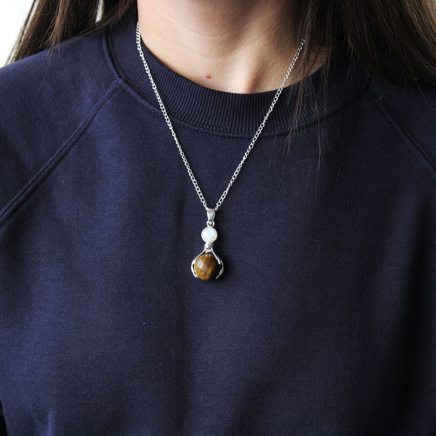 Hand-carved gemstone pendant featuring a Tiger Eye crystal sphere held by two silver-toned healing hands.