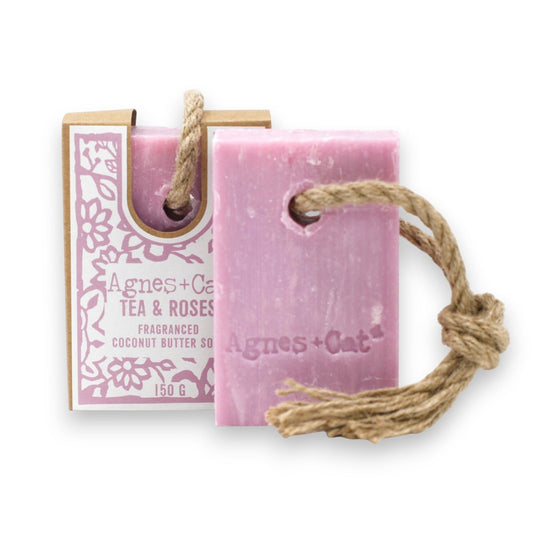 Large artisanal soap bar with an integrated hanging rope, featuring a textured surface in a natural floral setting.