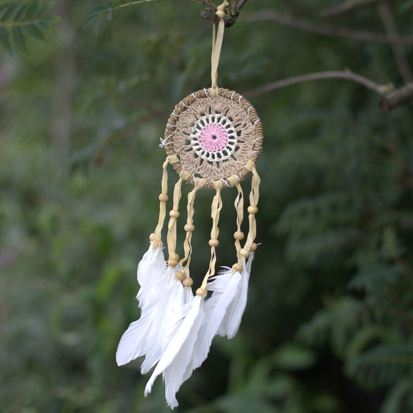 Small pastel pink macramé dream catcher featuring a woven web and hanging cotton tassels.