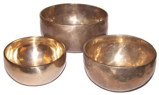 Three nested handmade brass singing bowls with a traditional golden finish on a neutral background.