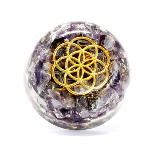 Clear resin orgonite dome containing purple amethyst gemstone chips, copper coils, and metal filings on a wooden surface.