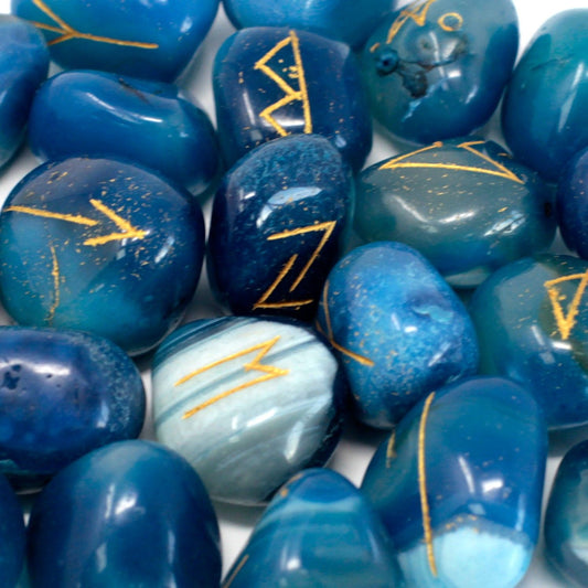 Hand-carved blue onyx rune stones with gold lettering spread next to a small blue drawstring pouch.