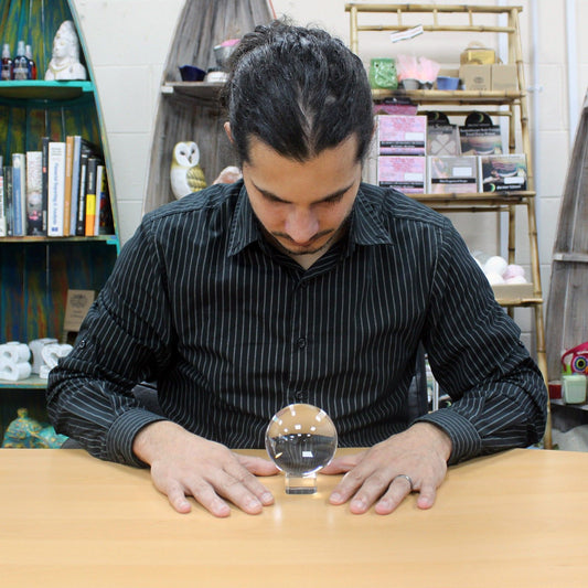 Clear 80mm optical glass crystal ball resting on a simple dark wooden stand against a neutral background.
