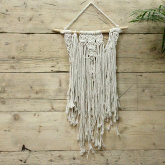 Intricate handcrafted cream macrame wall hanging with boho fringe and geometric woven patterns on a wooden dowel.