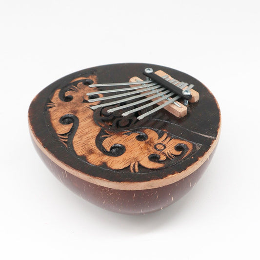 Handcrafted coconut shell thumb piano with seven steel keys and decorative carved patterns.