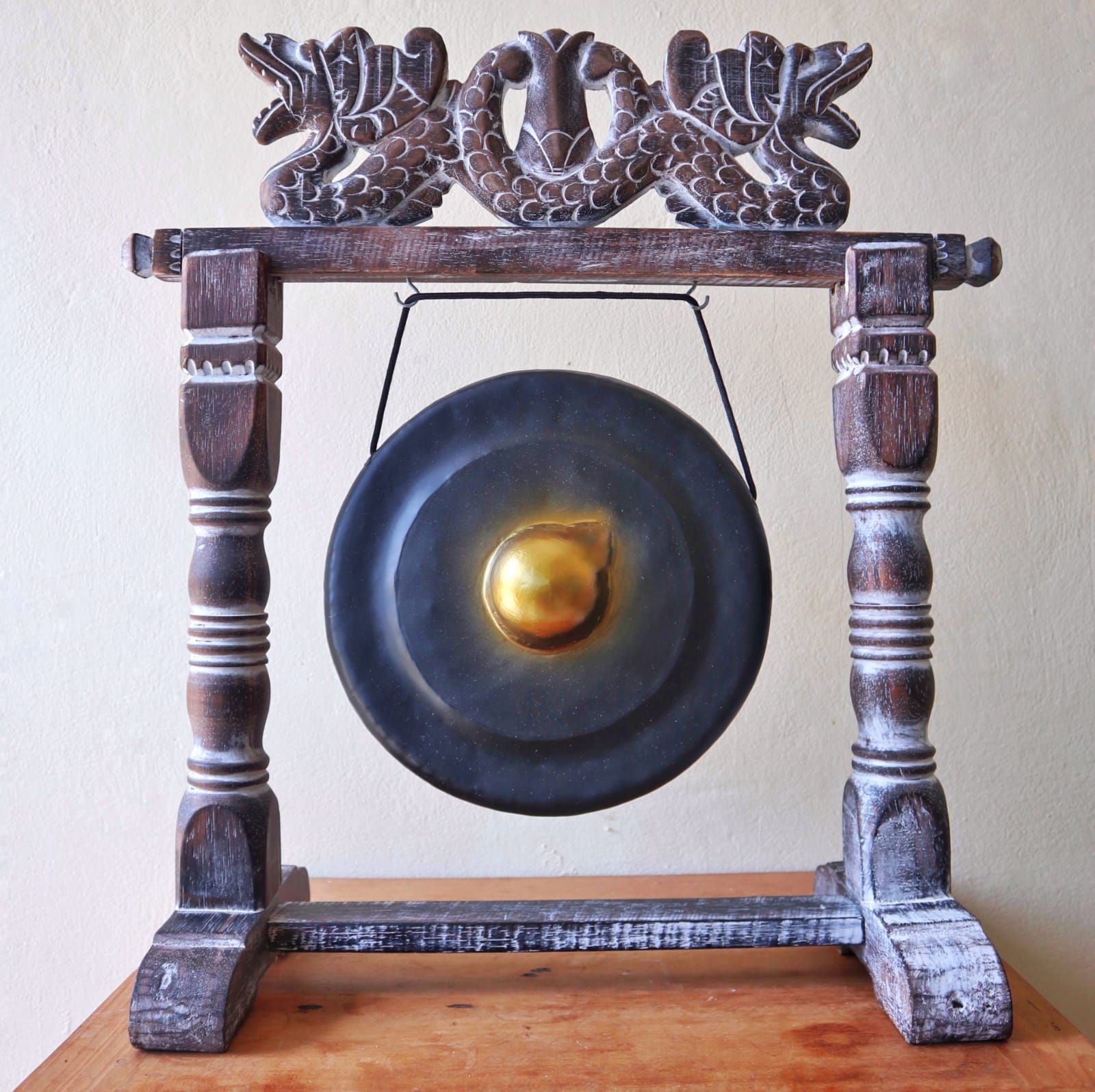 Small black healing gong hanging from a sturdy, decoratively carved wooden stand on a plain background.