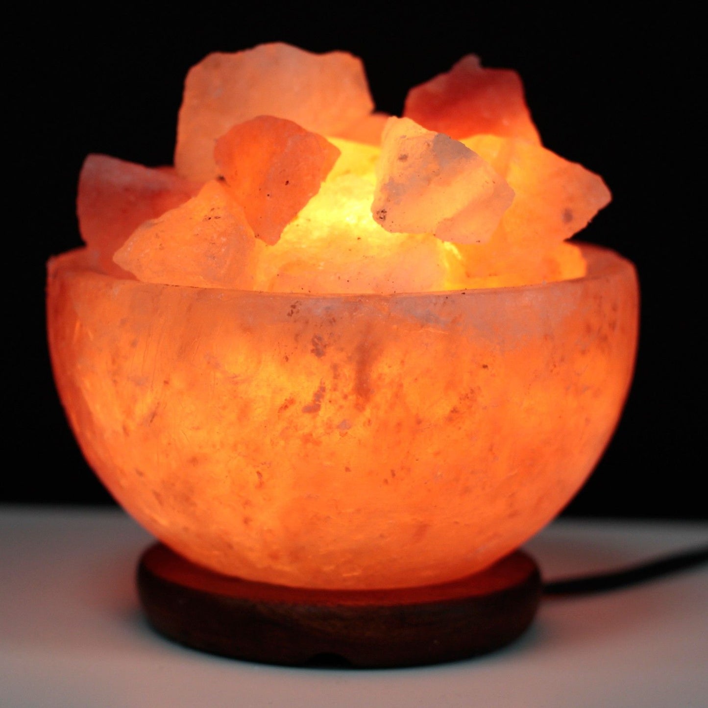 Hand-crafted pink Himalayan salt bowl filled with natural salt chunks, emitting a warm and soothing orange glow.