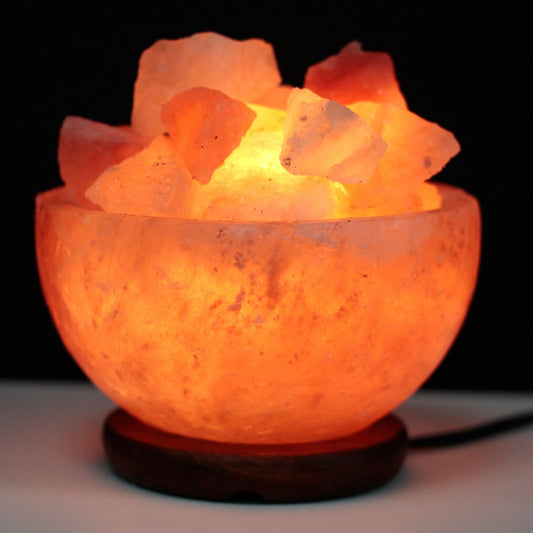 Hand-crafted pink Himalayan salt bowl filled with natural salt chunks, emitting a warm and soothing orange glow.