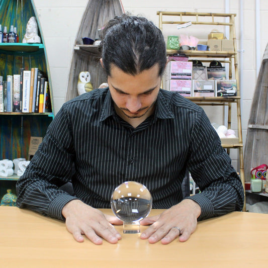 Clear 100mm optical glass crystal ball resting on a simple wooden stand, showing a reflected inverted view.
