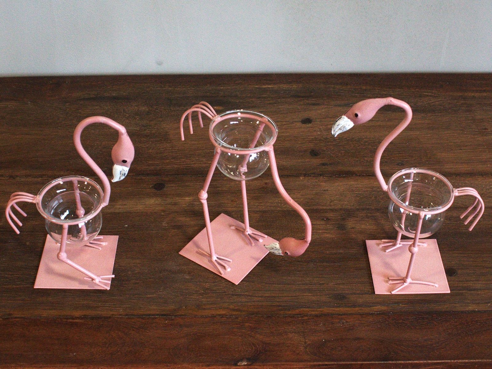 Charming pink metal flamingo stand holding a glass laboratory-style hydroponic test tube vase for plant propagation.