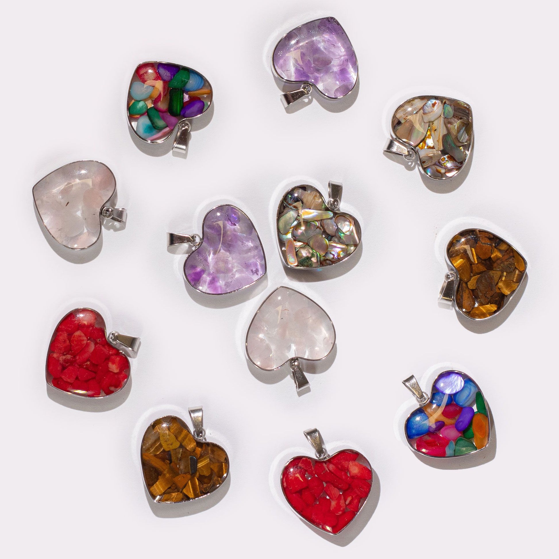 Heart-shaped steel pendant filled with colourful assorted gemstone chips and natural shells on a white background.
