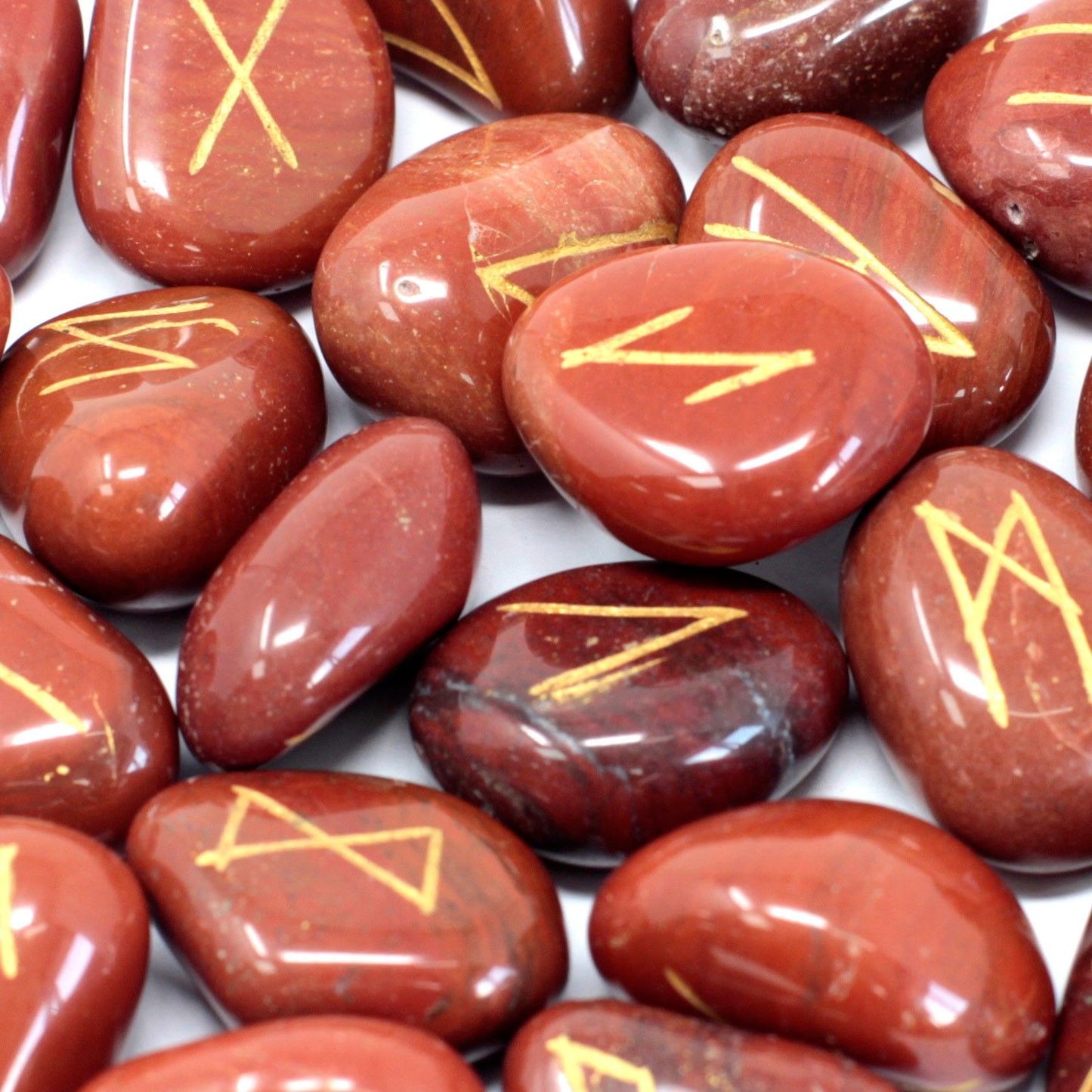 Tumbled red jasper stones engraved with gold rune symbols, scattered next to a small drawstring storage pouch.