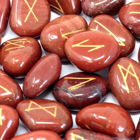 Tumbled red jasper stones engraved with gold rune symbols, scattered next to a small drawstring storage pouch.