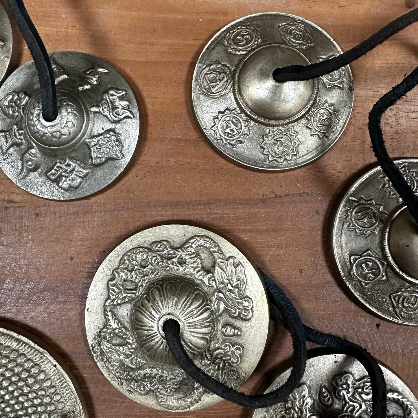 Small brass Tibetan tingsha bells embossed with traditional lucky symbols and joined by a leather cord.