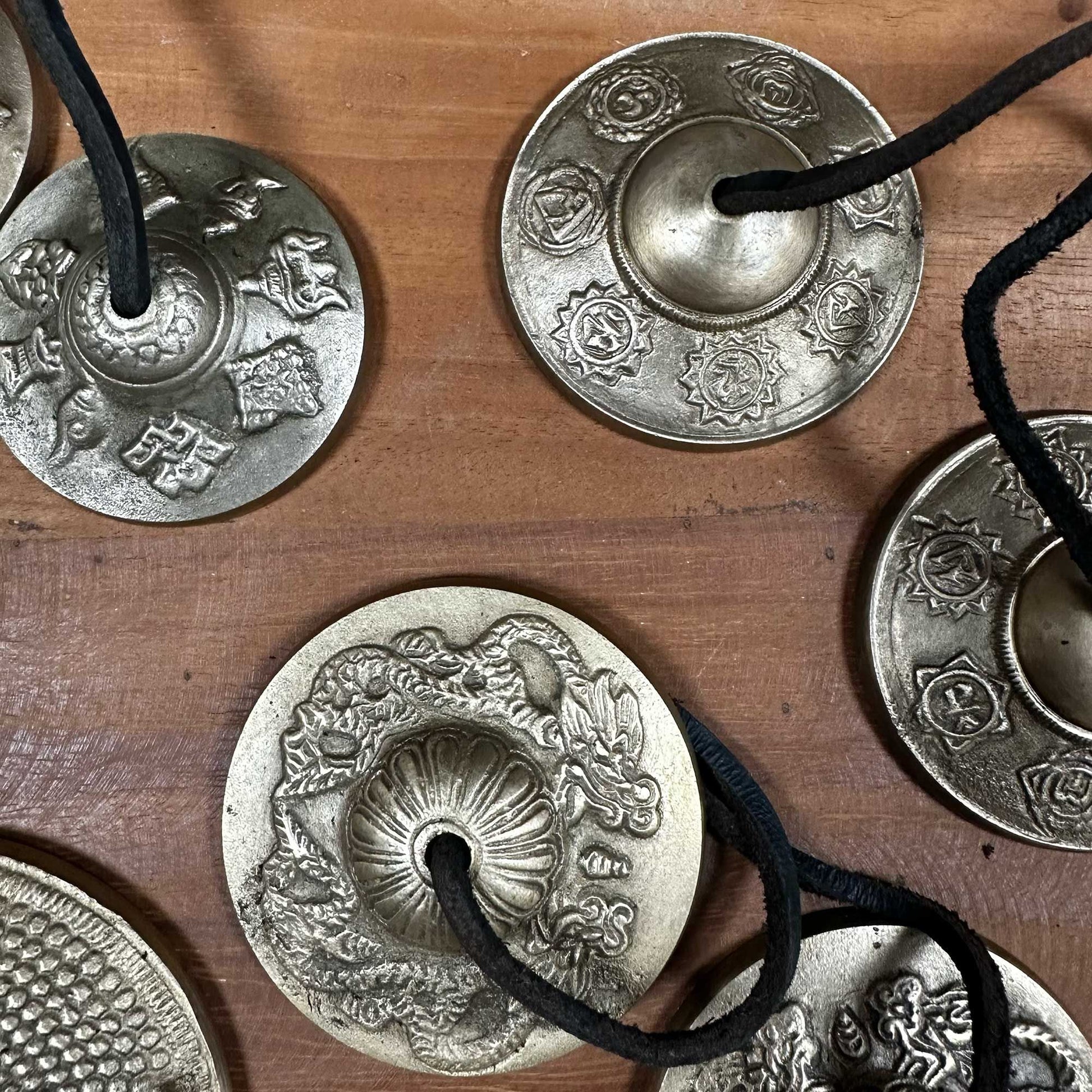 Small brass Tibetan tingsha bells embossed with traditional lucky symbols and joined by a leather cord.