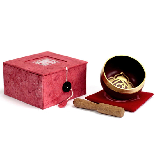 Handcrafted red root chakra singing bowl with a wooden striker on a decorative cushion.