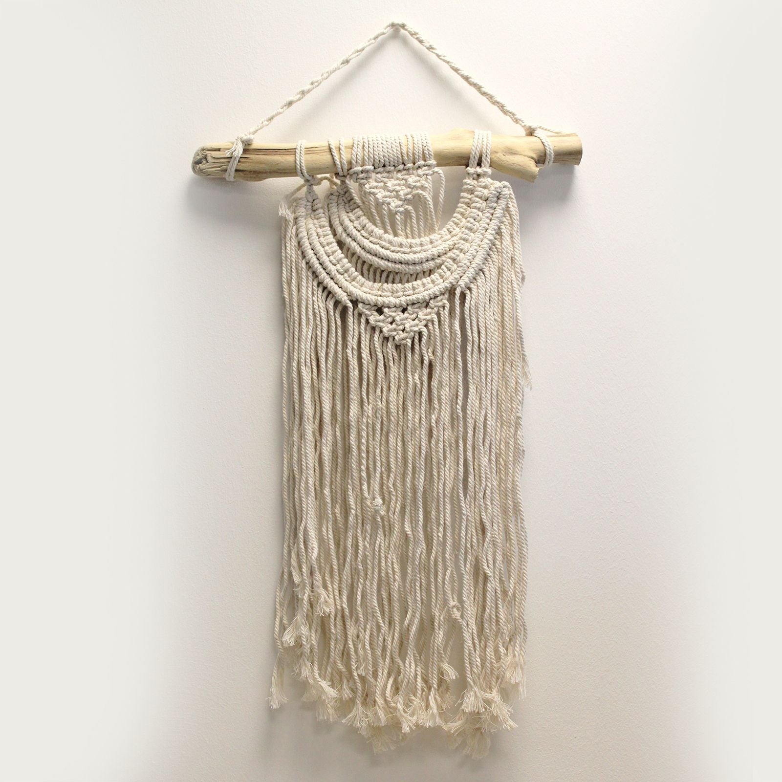 Handcrafted cream macrame wall hanging with a decorative double wave pattern and fringe on a wooden dowel.