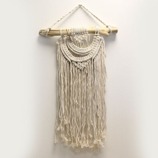 Handcrafted cream macrame wall hanging with a decorative double wave pattern and fringe on a wooden dowel.