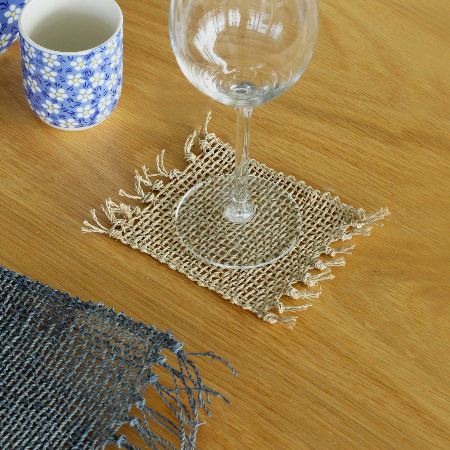 Set of four circular handwoven natural seagrass coasters featuring a decorative fringe edge detail.