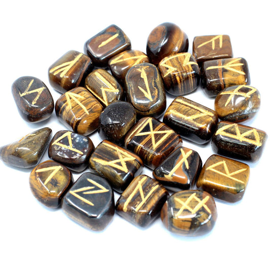 Golden brown Tiger Eye stones engraved with traditional rune symbols laid out next to a black drawstring pouch.