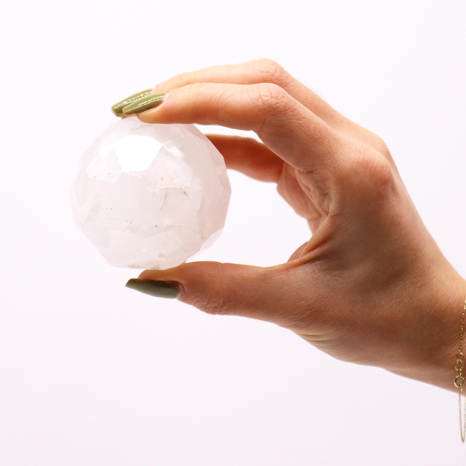 Clear faceted rock quartz gemstone sphere sitting on a light brown wooden stand.